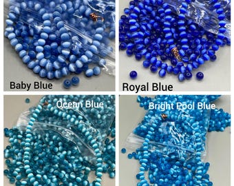 May include: Four bags of glass beads in different shades of blue. The bags are labeled "Baby Blue", "Royal Blue", "Ocean Blue", and "Bright Pool Blue".