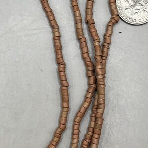 May include: Close-up of several strands of brown wooden beads. The beads are cylindrical and strung together, creating a necklace or bracelet. A US quarter is included for size reference.
