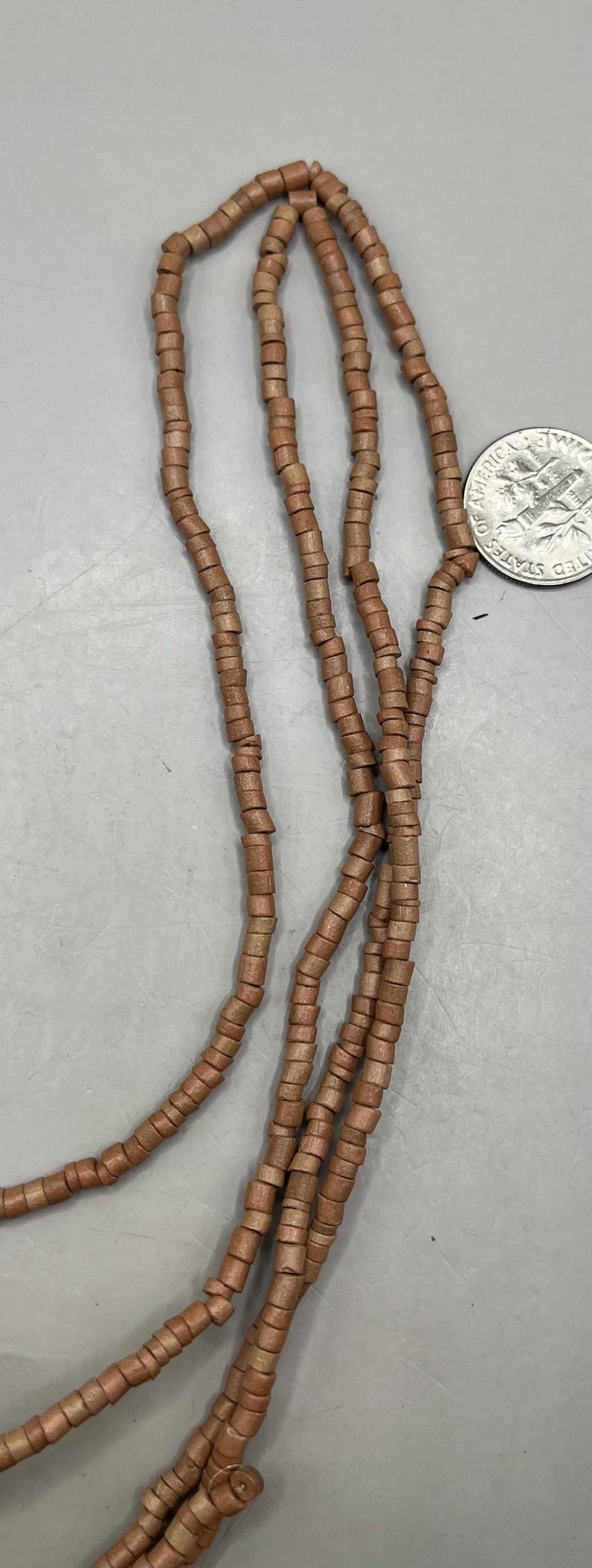 May include: Close-up of several strands of brown wooden beads. The beads are cylindrical and strung together, creating a necklace or bracelet. A US quarter is included for size reference.