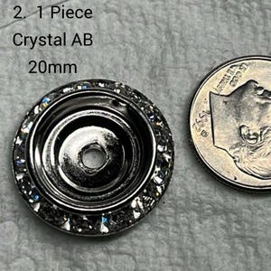 May include: A silver-colored crystal button with a ring of clear crystals around the edge. The text on the image reads "2. 1 Piece Crystal AB 20mm". A US dime is next to the button for size comparison.