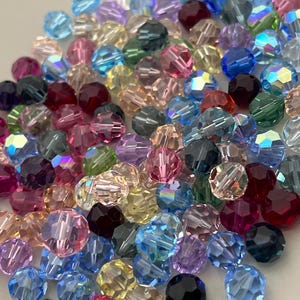 May include: A large assortment of colorful glass beads. The beads are round and have a faceted design. The beads are in various shades of blue, green, pink, purple, red, and yellow.