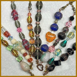 May include: A collection of five beaded strands featuring a variety of glass beads in assorted shapes, sizes, and colors including blue, orange, green, pink, and black. The strands incorporate textured, metallic, and clear glass elements.
