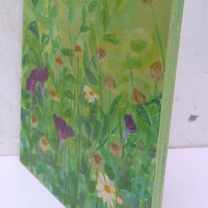 May include: A painting of a field of wildflowers in shades of green, purple, and white. The flowers are painted in a loose, impressionistic style.