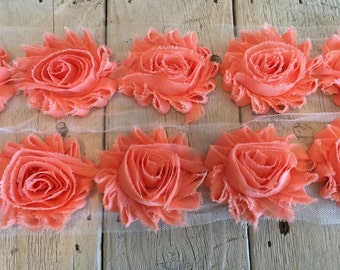 May include: Peach colored fabric flower trim with a white mesh backing. The trim is made of multiple layers of fabric to create a 3D flower effect.
