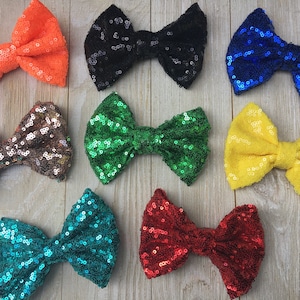 May include: Assortment of ten sequined hair bows in various colors, including orange, black, blue, gold, green, teal, and red.