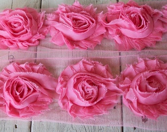 May include: Pink fabric rose trim with a delicate tulle backing. The trim features a row of large, ruffled fabric roses.