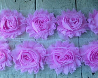 May include: A strip of pink fabric flowers on a white mesh background. The flowers are made of soft, ruffled fabric and have a delicate, feminine look.
