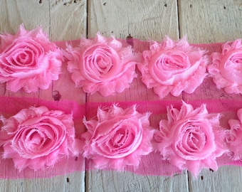 May include: Pink fabric flower trim with a ruffled design. The trim is on a pink mesh background.
