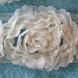 May include: White fabric flower with a ruffled texture. The flower is made of multiple layers of fabric and has a delicate, feminine look.