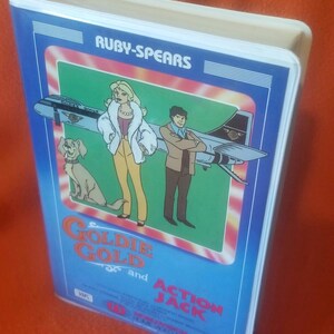 May include: A vintage VHS tape for the animated series "Goldie Gold and Action Jack." The cover features cartoon illustrations of the characters, a dog, and a jet plane, set against a blue background with the title text.