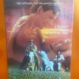 Peut inclure: Une cassette VHS du film Thousand Pieces of Gold avec une couverture aux tons de coucher de soleil, un grand portrait d'un homme et d'une femme, une scène équestre et le texte One Of The Best Films Of The Year et Not Rated.