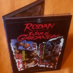 Peut inclure: Un boîtier DVD noir de la collection Toho Master, présentant le film "Rodan and War of the Gargantuas". La couverture comprend des images de monstres et du texte japonais. Le boîtier est ouvert, révélant le disque à l'intérieur.