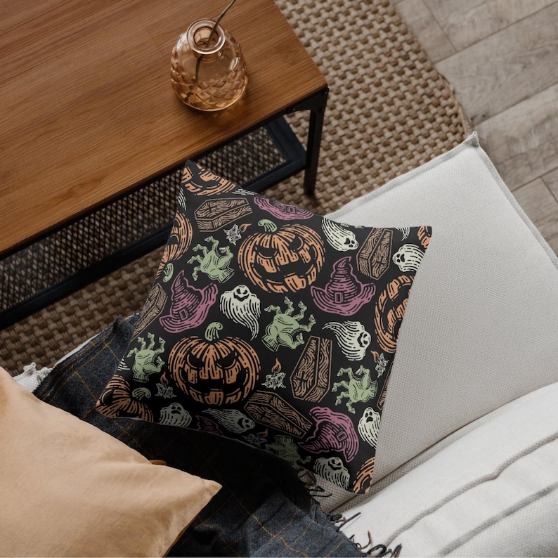 May include: A decorative Halloween-themed pillow with a black background. The pillow features a repeating pattern of jack-o'-lanterns, witch hats, ghosts, coffins, and zombie hands in orange, green, pink, and white.