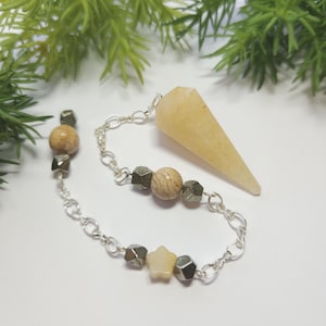 May include: A pendulum featuring a pointed, light yellow stone crystal attached to a silver-toned metal chain. The chain is decorated with round, tan-colored stone beads, small metallic cubes, and a single light yellow stone star-shaped charm.