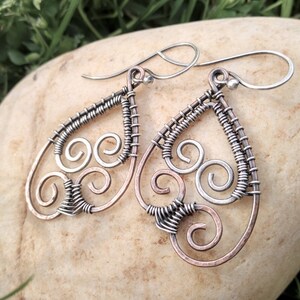 May include: A pair of silver and copper wire earrings with a teardrop shape and a swirling design.
