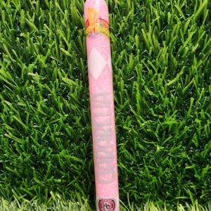 May include: A pink glitter pen with the word "Ranger" in silver lettering. The pen features a white diamond shape and a colorful graphic. The pen is set against a backdrop of green artificial grass.