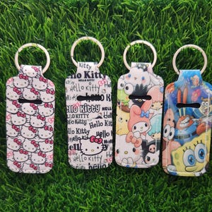 May include: Six keychains with silver rings, each featuring a different design. The designs include Snoopy, Hello Kitty, and characters from SpongeBob SquarePants. The keychains are rectangular with a black cutout.