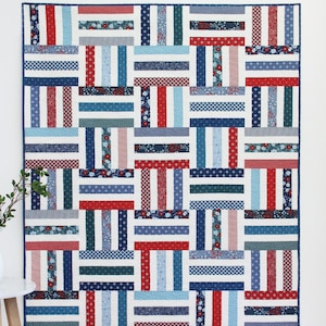 Puede incluir: Un edredón de patchwork con un diseño geométrico, con telas rojas, blancas y azules. El edredón tiene un patrón de rayas con varias estampados florales y de lunares. Las palabras "Strip Flip" y "A jelly roll friendly quilt in 5 sizes" son visibles.