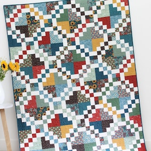 Può includere: Una colorata trapunta con un design patchwork, con quadrati di vari modelli e colori, tra cui stampe rosse, blu, gialle e floreali. La trapunta è etichettata "Honeycrisp" e "Chick Cluck Sew". È visibile anche il testo "Fat Quarter and strip friendly in 5 sizes".