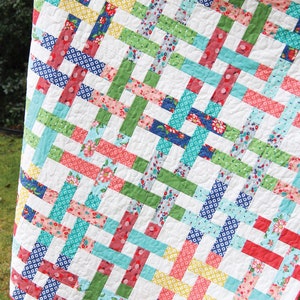 May include: A colorful quilt with a woven basket design. The quilt features a variety of patterned fabrics in red, blue, green, and yellow, set against a white background. The text "Basket Case" and "Jelly Roll Friendly" are visible.