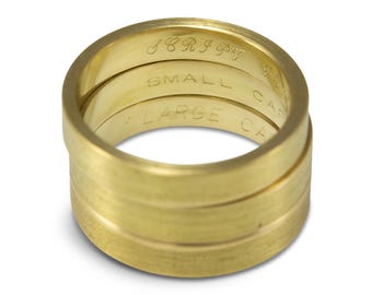May include: Three gold rings stacked on top of each other. The top ring has the word "SCRIPT" engraved on it. The middle ring has the word "SMALL CAPS" engraved on it. The bottom ring has the word "LARGE CAPS" engraved on it.