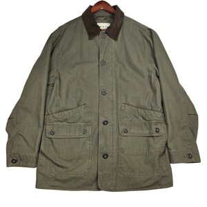 May include: An olive green field jacket featuring a dark brown corduroy collar, a button-front closure, and four large front pockets with buttoned flaps. The interior label displays the brand name Orvis. The jacket has long sleeves with buttoned cuffs.