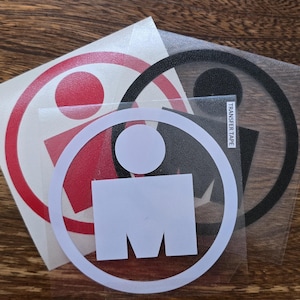 May include: A collection of Ironman logo stickers in red, white, and black. The stickers feature the iconic Ironman symbol: a circle with a dot and a stylized figure. The stickers are on a clear backing, ready for application.
