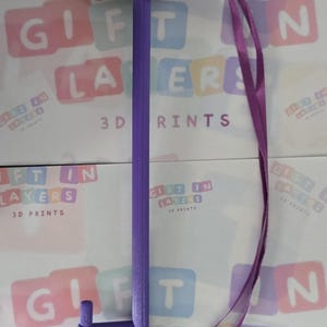 May include: A purple plastic tool with a handle and a hook on the end. The tool is attached to a purple lanyard. The tool is labeled "Gift in Layers 3D Prints".