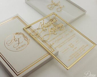 May include: A gold-framed clear acrylic wedding invitation with the couple's names "Alana & Jeremy" in elegant calligraphy. The invitation includes the date, time, and location of the wedding ceremony. The text reads "Together with their families, Alana & Jeremy request your presence to honor their love in ceremony on Saturday, July 22, 2023 at 4pm. The Willow Glass House, The Oak Atelier - 15475 Pin Oak Dr, Conroe, TX, 77334."