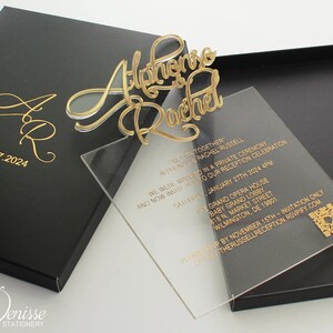 May include: A clear acrylic wedding invitation with gold lettering. The invitation reads "We were married in a private ceremony, and now invite you to our reception celebration Saturday, January 27th, 2024, 4 PM. The Grand Opera House, Baby Grand Lobby, 818 N. Market Street, Wilmington, DE 19801. Please RSVP by November 15th - Invitation Only.  GuestHerRussellReception.RSVPify.com"