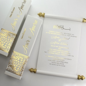 Puede incluir: Invitación de boda en rollo blanco con caligrafía dorada. El rollo está enrollado y atado con una cinta dorada. La invitación dice "Amir & Amera" e incluye la fecha, la hora y el lugar de la boda. La invitación también incluye el texto "No se aceptan regalos en caja, por favor."