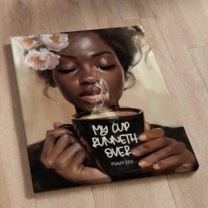 May include: Canvas art print featuring a Black woman with flowers in her hair, holding a black mug with the text "My Cup Runneth Over" and Psalm 23:5. The artwork has a warm color palette.