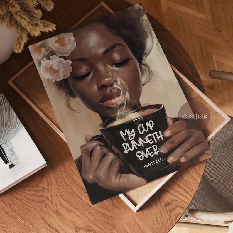 May include: An art print featuring a woman with dark skin holding a black mug with the text "MY CUP RUNNETH OVER" and "PSALM 23:5". The woman has flowers in her hair and steam rising from the mug. The print is on a wooden tray.
