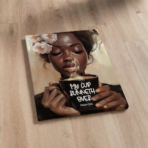 May include: A canvas print featuring a portrait of a person with closed eyes, holding a black mug with the text "My cup runneth over" and "Psalm 23:5". The person has flowers in their hair and steam rising from the mug.