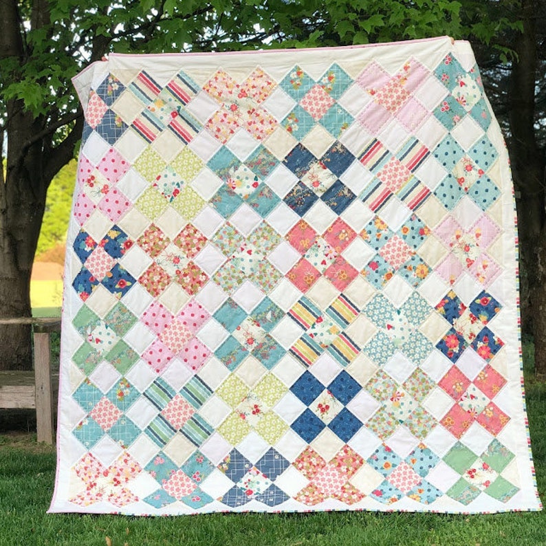 Puede incluir: Una colcha blanca con un dise&ntilde;o de patchwork que presenta una variedad de patrones florales en tonos de rosa, azul, verde y amarillo. La colcha est&aacute; compuesta por cuadrados con un patr&oacute;n de cruz en el centro.