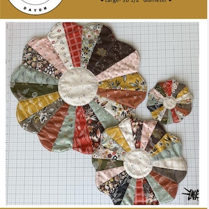 May include: A sewing pattern for Grandmother's Sunburst designs. The image shows three colorful, flower-shaped quilted items in various sizes: 5-inch, 11-inch, and 16.5-inch diameters. The pattern is by Jessica Dayon.