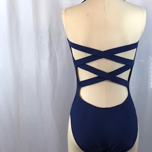 May include: A navy blue leotard with a criss-cross back design. The leotard has a halter neckline and a high leg cut.
