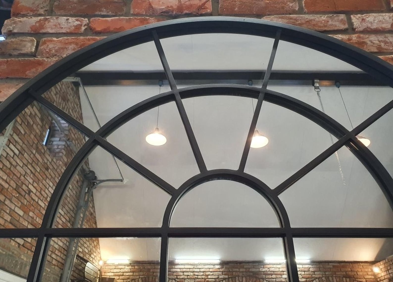 Detail view of large arched dungeon mirror with steel frame, perfect for enhancing sex dungeon depth and visibility