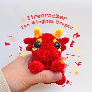 Può includere: Un giocattolo di drago rosso all'uncinetto con corna gialle e grandi occhi neri. Il drago è etichettato "Firecracker The Wingless Dragon".