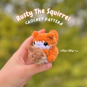 May include: A crocheted squirrel toy in shades of orange, white, and brown, holding a brown acorn. The text "Rusty The Squirrel CROCHET PATTERN" is displayed above the squirrel, with "LOW-SEW ~" below.