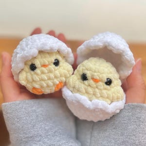 May include: Two crocheted yellow chicks with orange beaks and black eyes, each nestled in a white crocheted eggshell. The chicks are handmade and appear soft, perfect for Easter or spring decor.