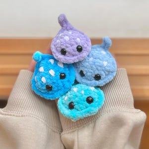 May include: Four crocheted plush stingray toys in shades of blue and purple. The stingrays have white spots and black eyes.