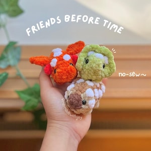 Pode incluir: Três pequenos brinquedos de pelúcia feitos de crochê, incluindo um peixe laranja brilhante com manchas brancas, um triceratops verde claro e um anquilossauro bege com marcas marrons. O texto FRIENDS BEFORE TIME e no-sew são visíveis.