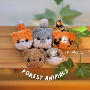 May include: A selection of handmade, no-sew crochet forest animal toys, including a fox, bear, tiger, hamster, and guinea pig. The toys are orange, brown, grey, and white, with black eyes. The text "FOREST ANIMALS" is visible.