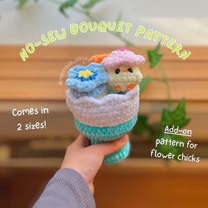 May include: A crocheted bouquet featuring a blue flower, an orange flower, and a chick wearing a pink hat. The bouquet is held in a turquoise, white, and blue vase. Text on the image reads "NO-SEW BOUQUET PATTERN" and "Comes in 2 sizes!"