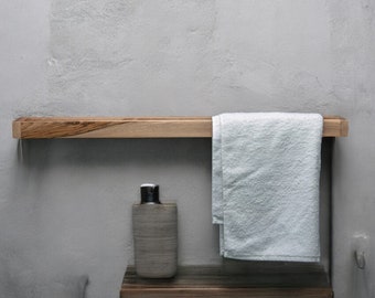 May include: A wooden shelf with a white towel hanging on it. A brown bottle with a black cap is on the shelf below the towel.