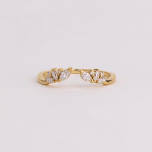 May include: A gold open ring featuring two symmetrical clusters of marquise-cut and round-cut clear stones. The band is polished gold, and the decorative elements are arranged in a leaf-like pattern on each side of the open center gap.