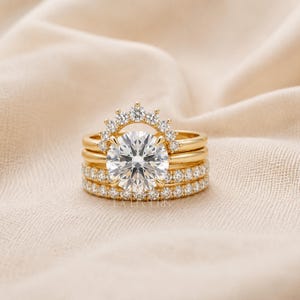 May include: A gold ring set consisting of three stacked bands. The centre band features a large round brilliant-cut clear stone, topped with a curved arch of smaller stones. The bottom band is a full eternity band set with small clear stones.