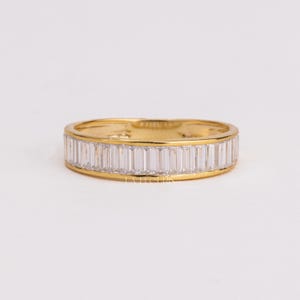 May include: A gold band ring featuring a continuous row of clear, rectangular baguette-cut stones set horizontally around the entire circumference. The metal has a polished finish, and the text LA EL CUPIS is visible on the inner band surface.