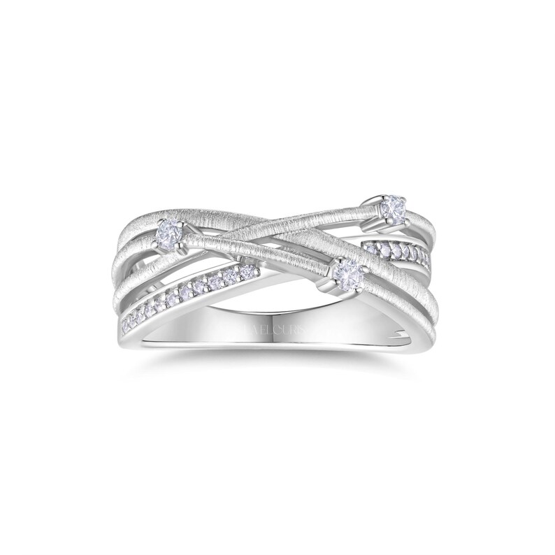 Puede incluir: Un anillo plateado con un dise&ntilde;o entrecruzado. El anillo presenta m&uacute;ltiples bandas, algunas adornadas con peque&ntilde;as gemas transparentes. Tres gemas m&aacute;s grandes est&aacute;n engastadas a intervalos. Fondo blanco.